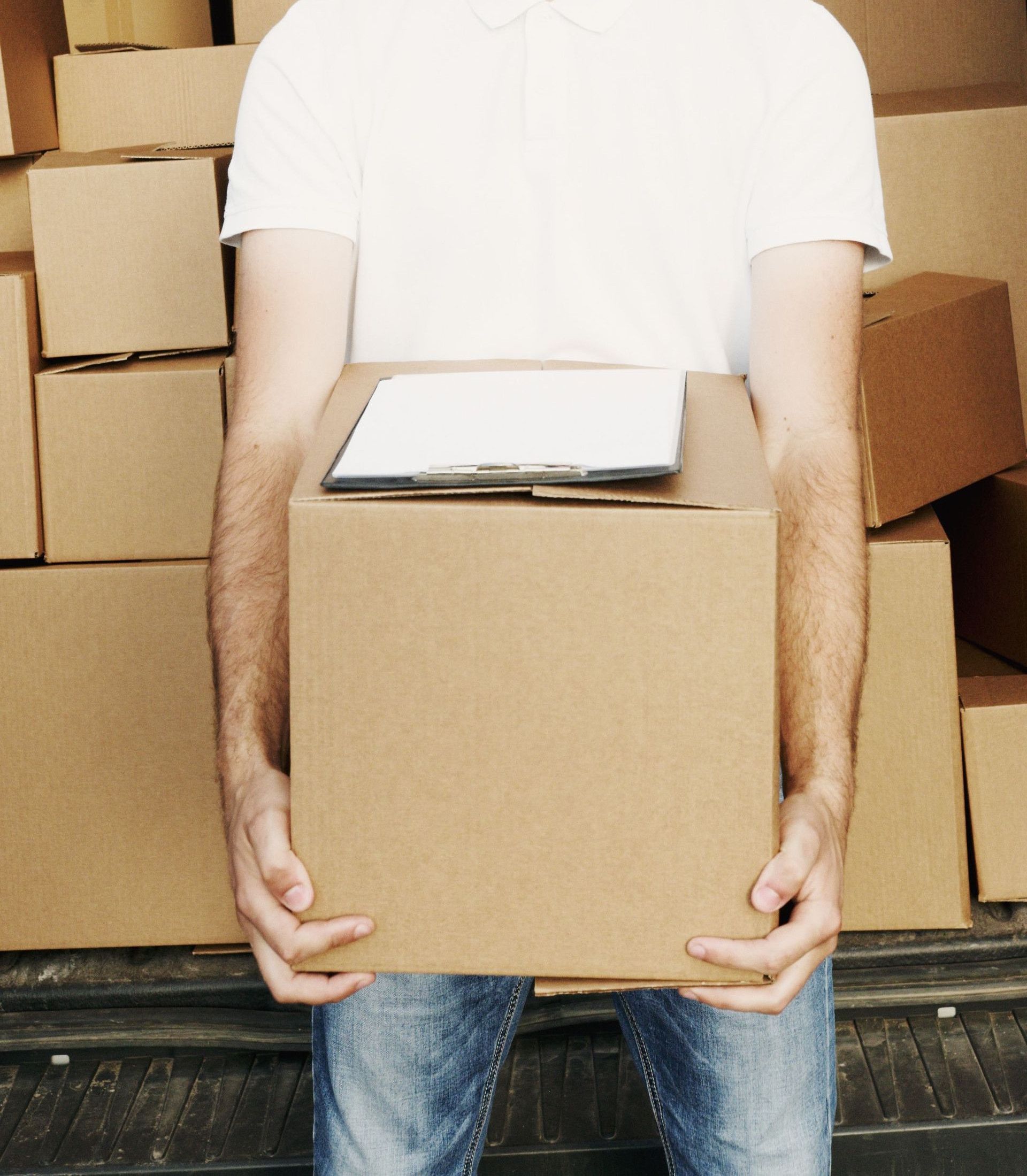 A deliveryman in a cap holding a box standing in front of a truck loaded with cartons.